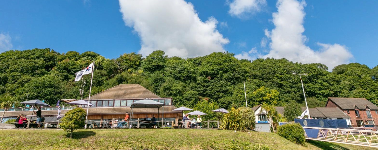 The Bar & Restaurant at Neyland Yacht Haven — timber building with a covered terrace above the marina, wooded hillside behind